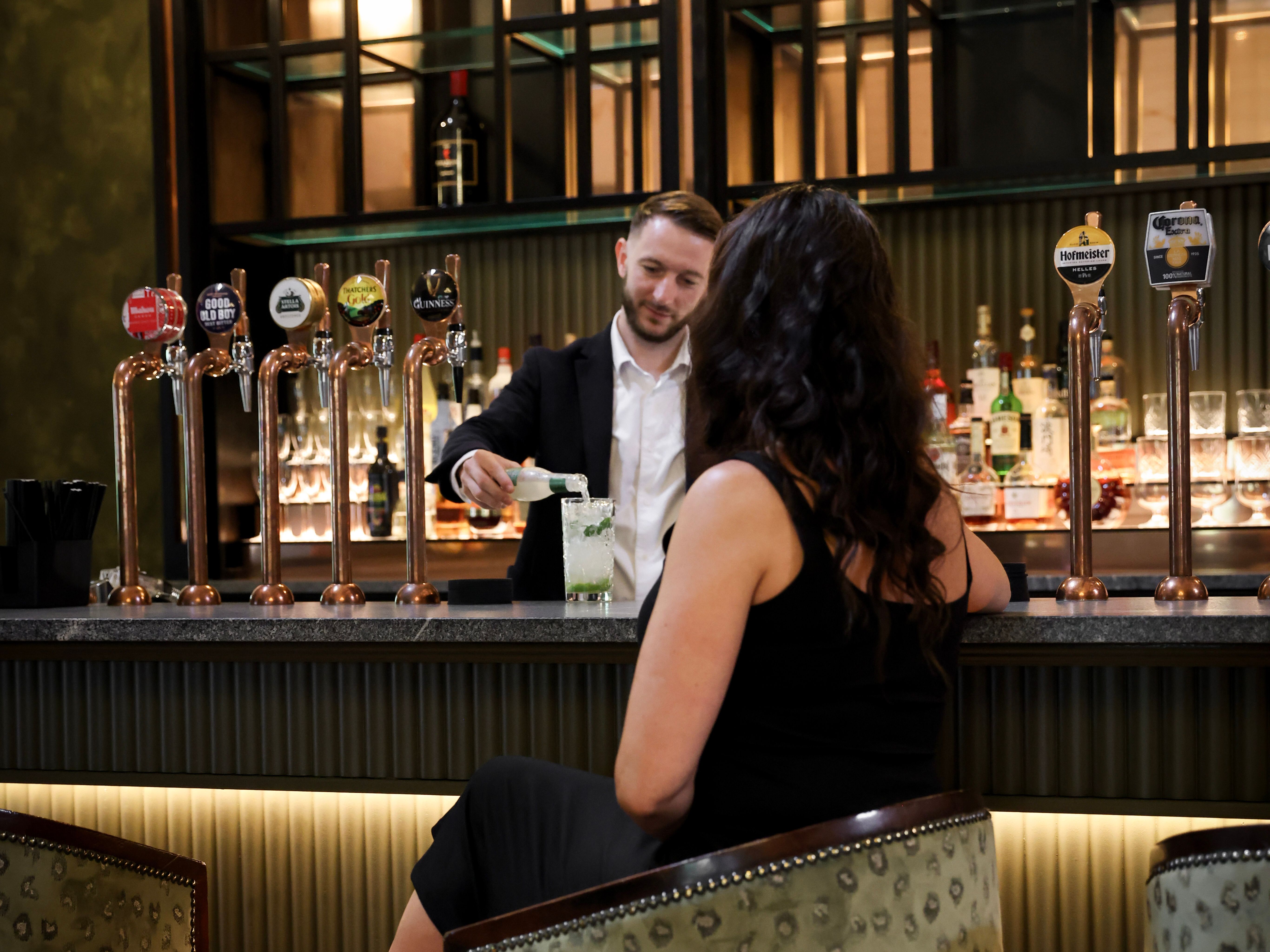 Bartender serving a cocktail to a woman sitting at a bar.