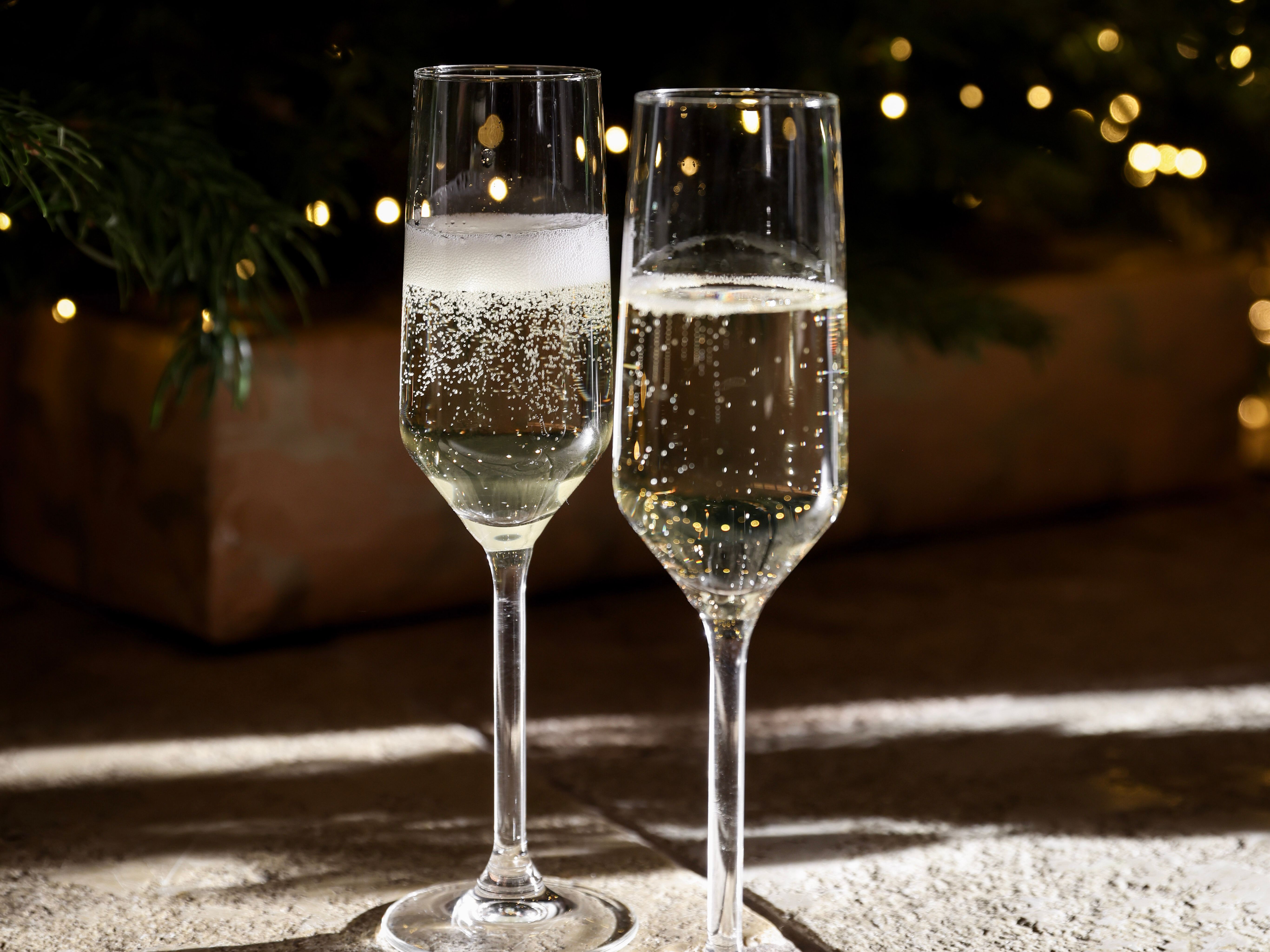 Champagne being poured into two flutes in front of a decorated Christmas tree