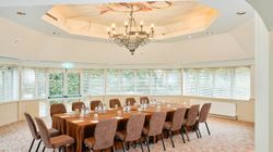 Conference room with a large rectangular table, brown chairs, water bottles, and a chandelier overhead