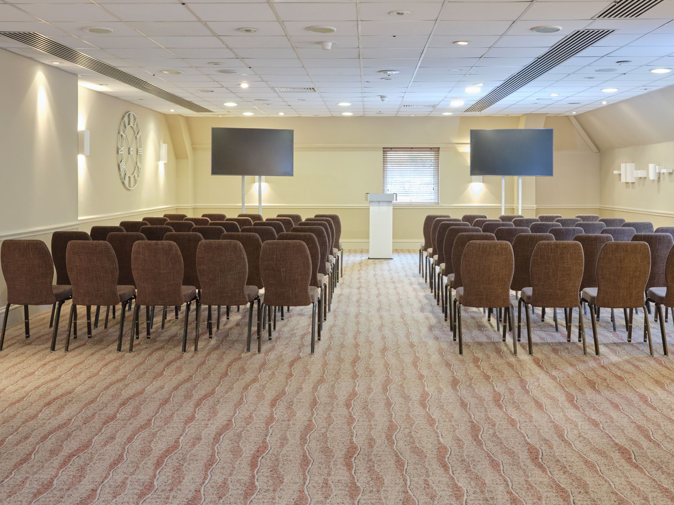 Conference room set up with rows of chairs facing a podium and two large screens.