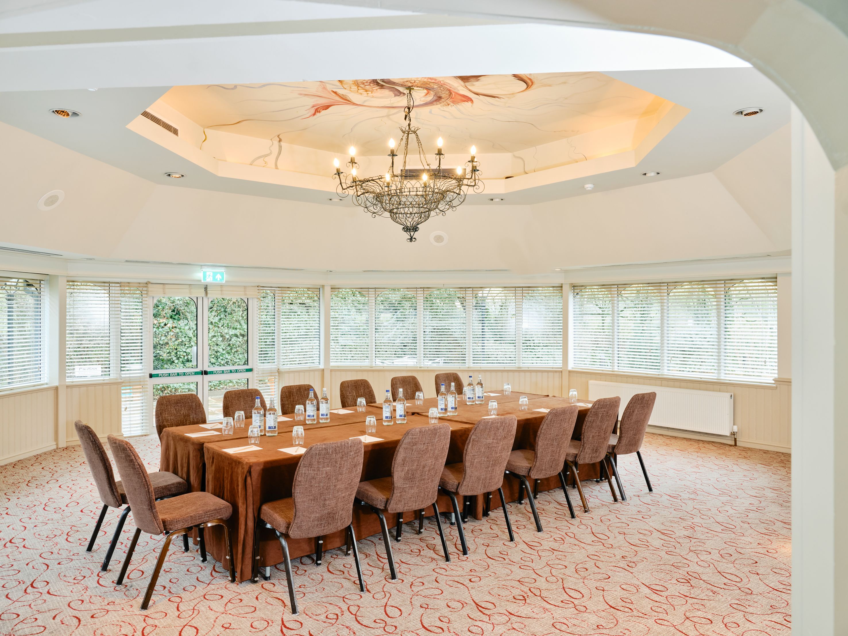 Conference room with a large table surrounded by chairs, set up with water bottles and glasses under a decorative chandelier