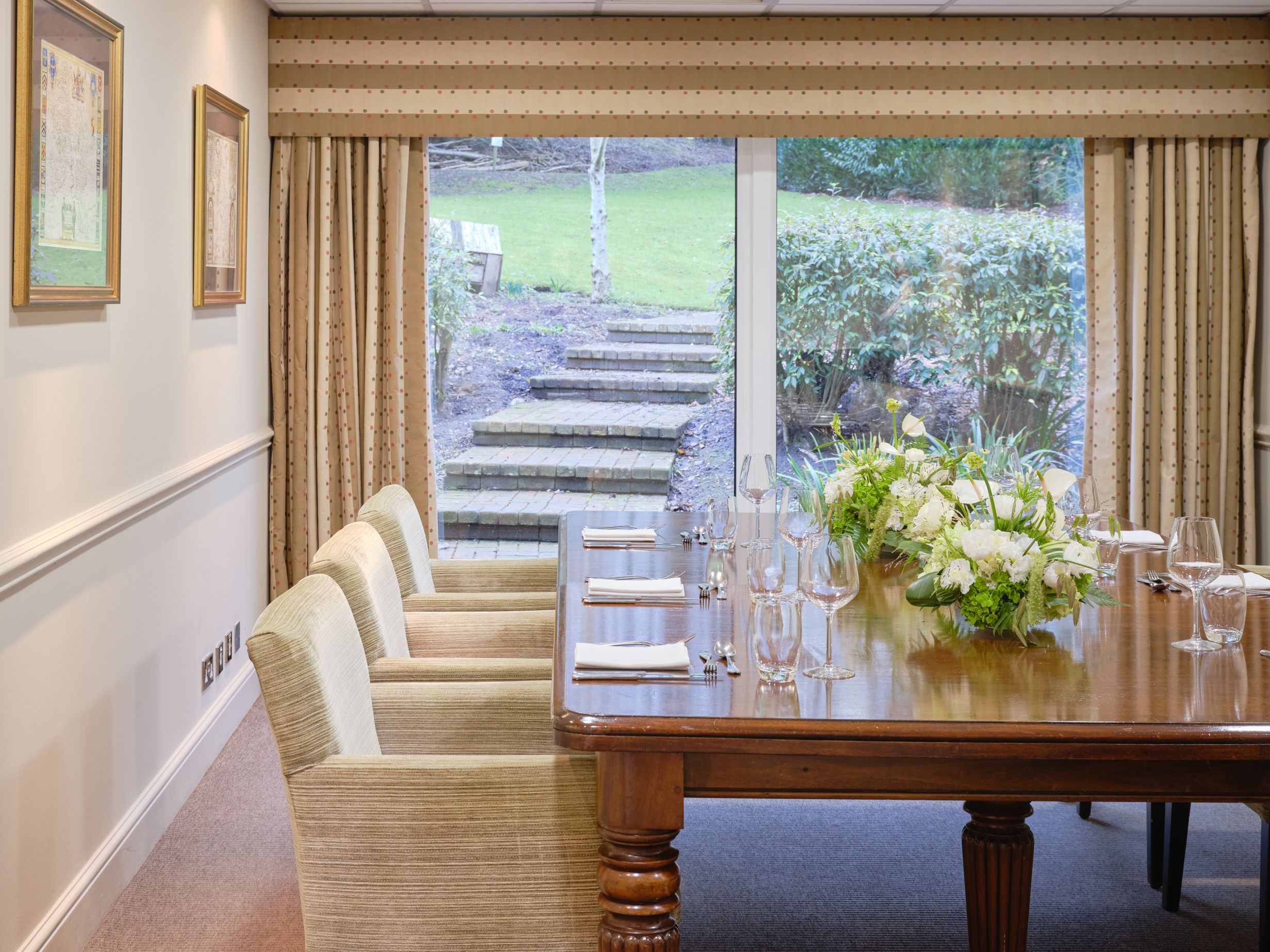 Elegant conference room with a wooden table, chairs, floral centerpiece, and view of garden steps through large window