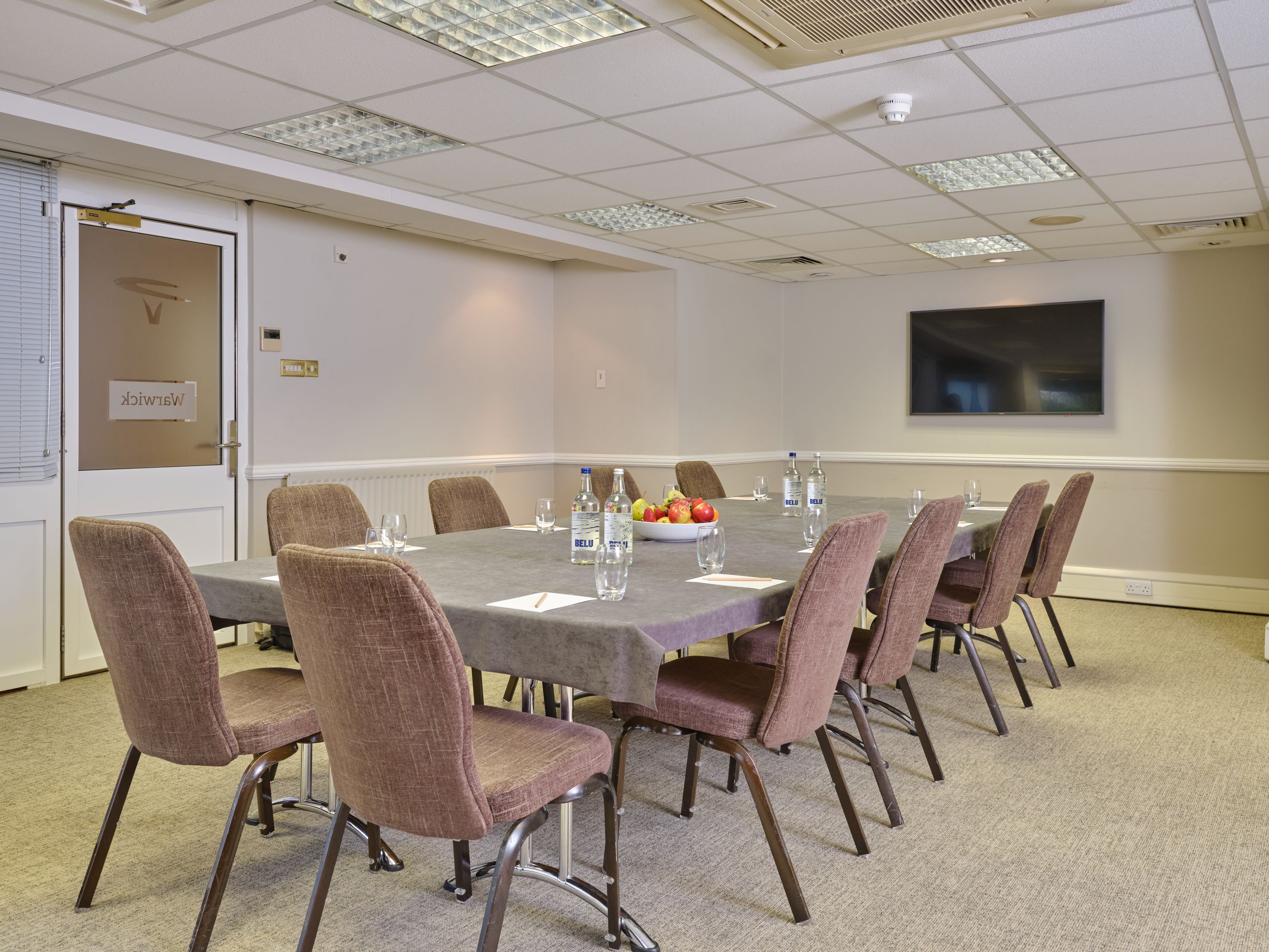 Modern conference room with rectangular table, chairs, notepads, water bottles, and a bowl of fruit.
