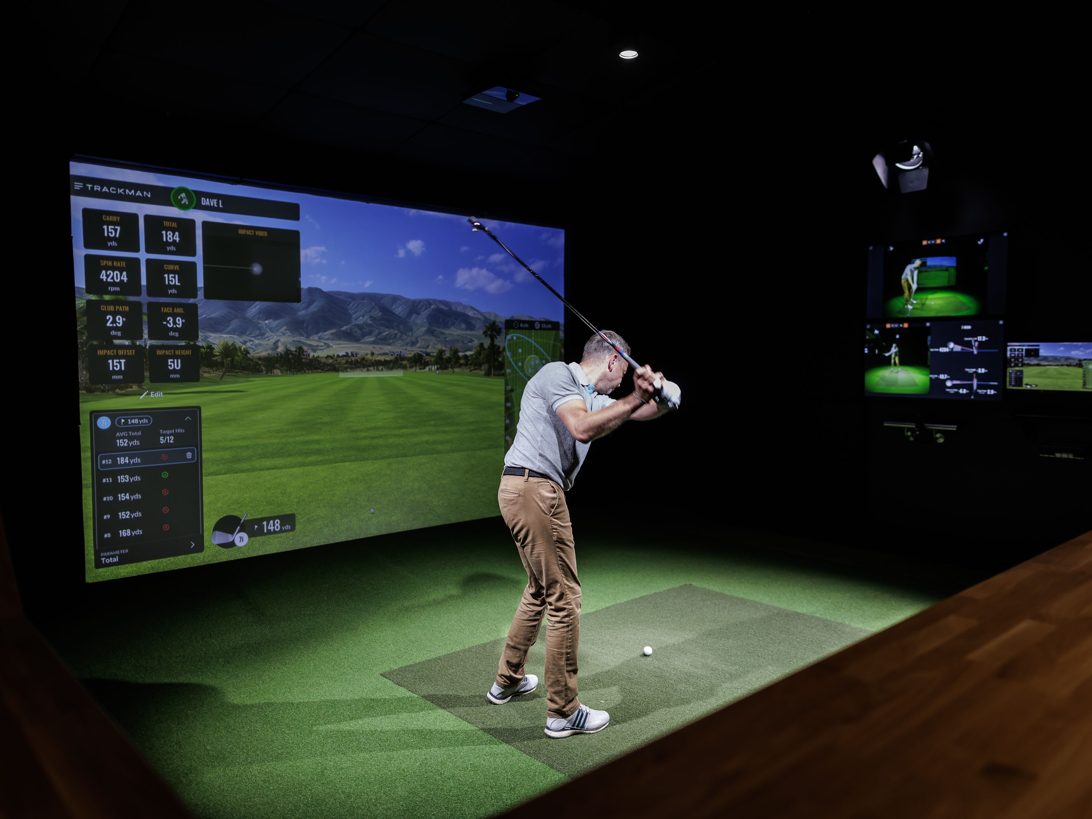 Man playing golf in an indoor golf simulator with virtual course and performance data displayed on the screen.