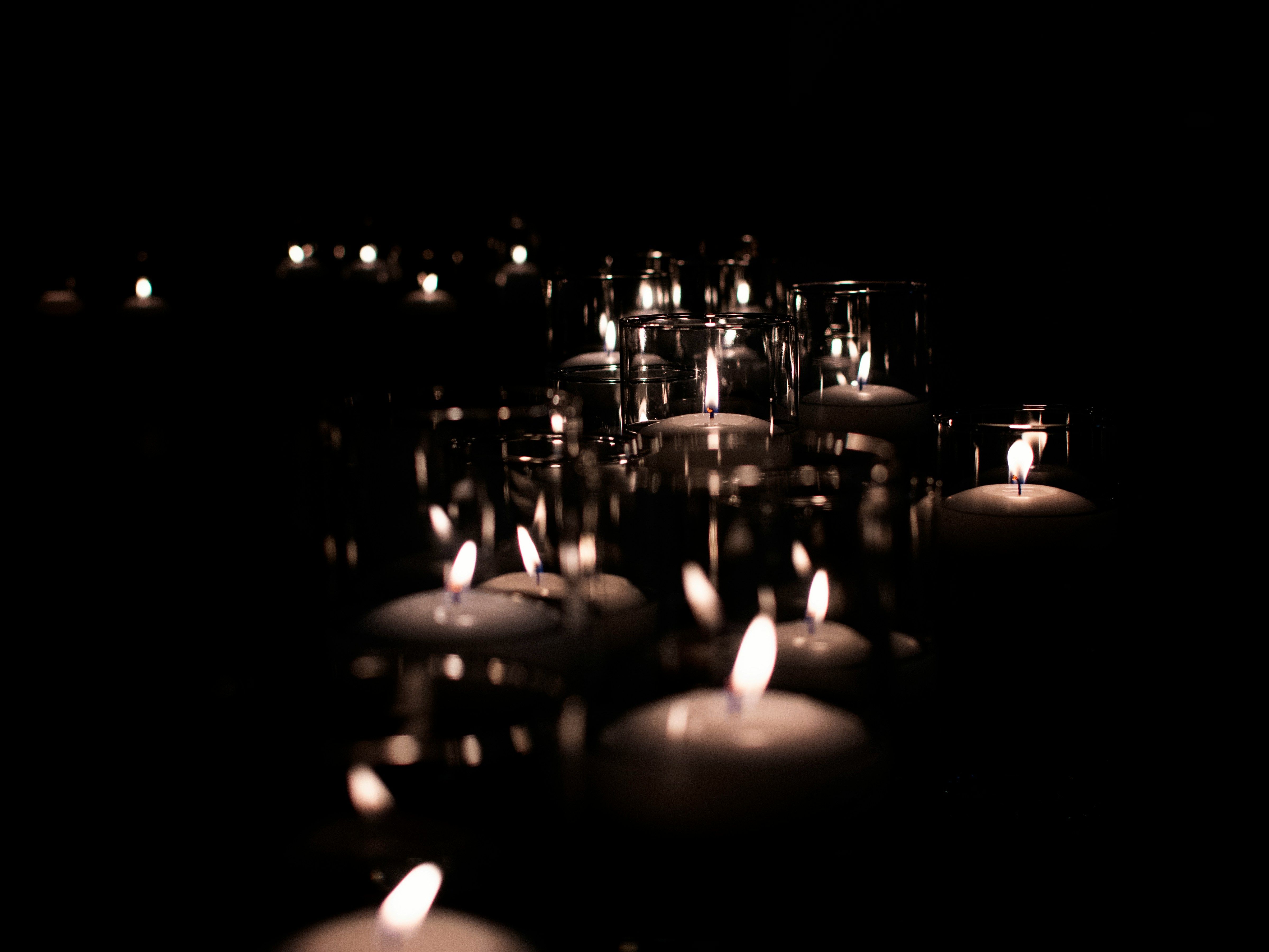 Multiple lit candles in glass holders glowing in the dark