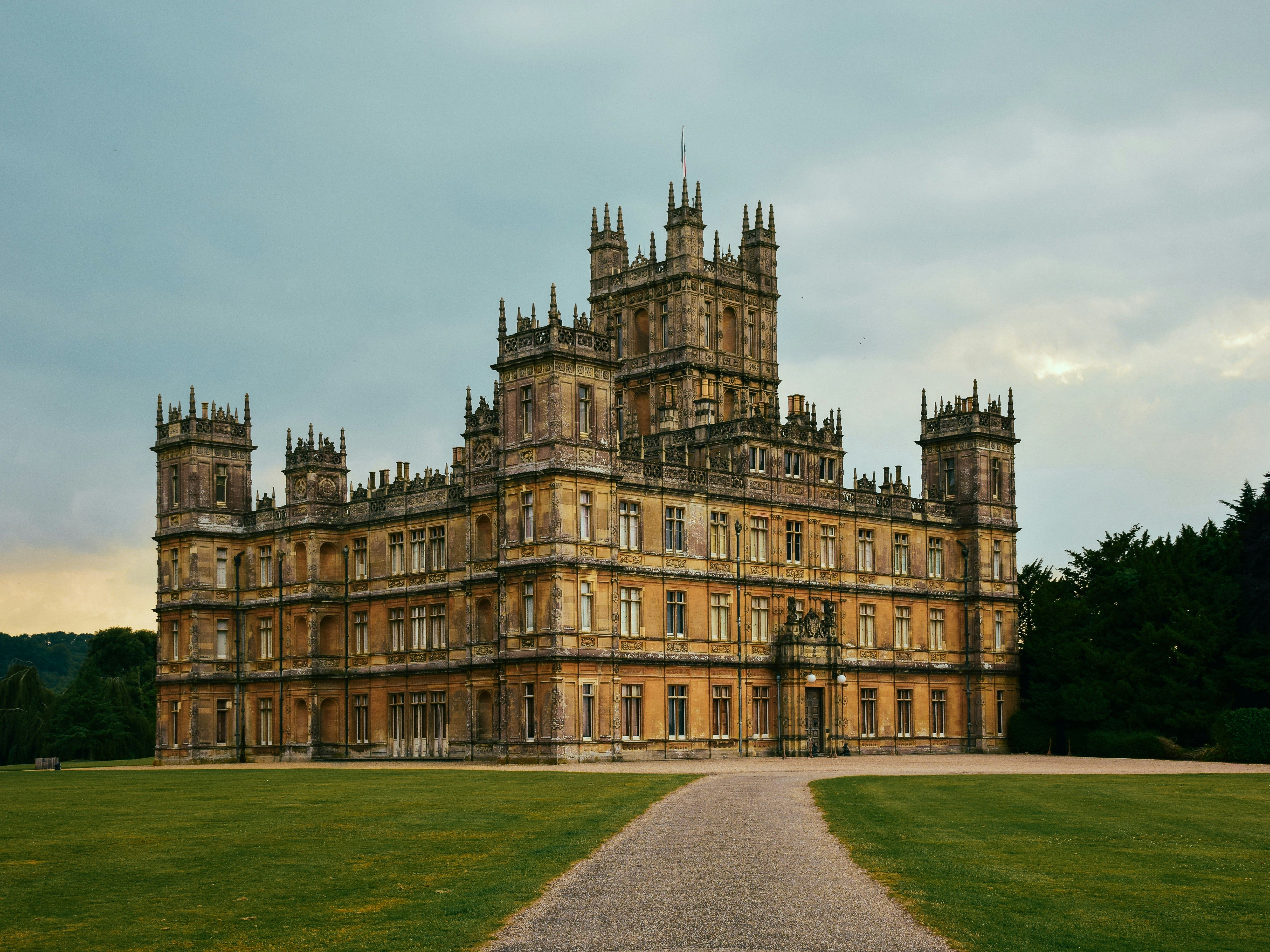 Large, historic castle with ornate architectural details and a central tower surrounded by lawn and trees.
