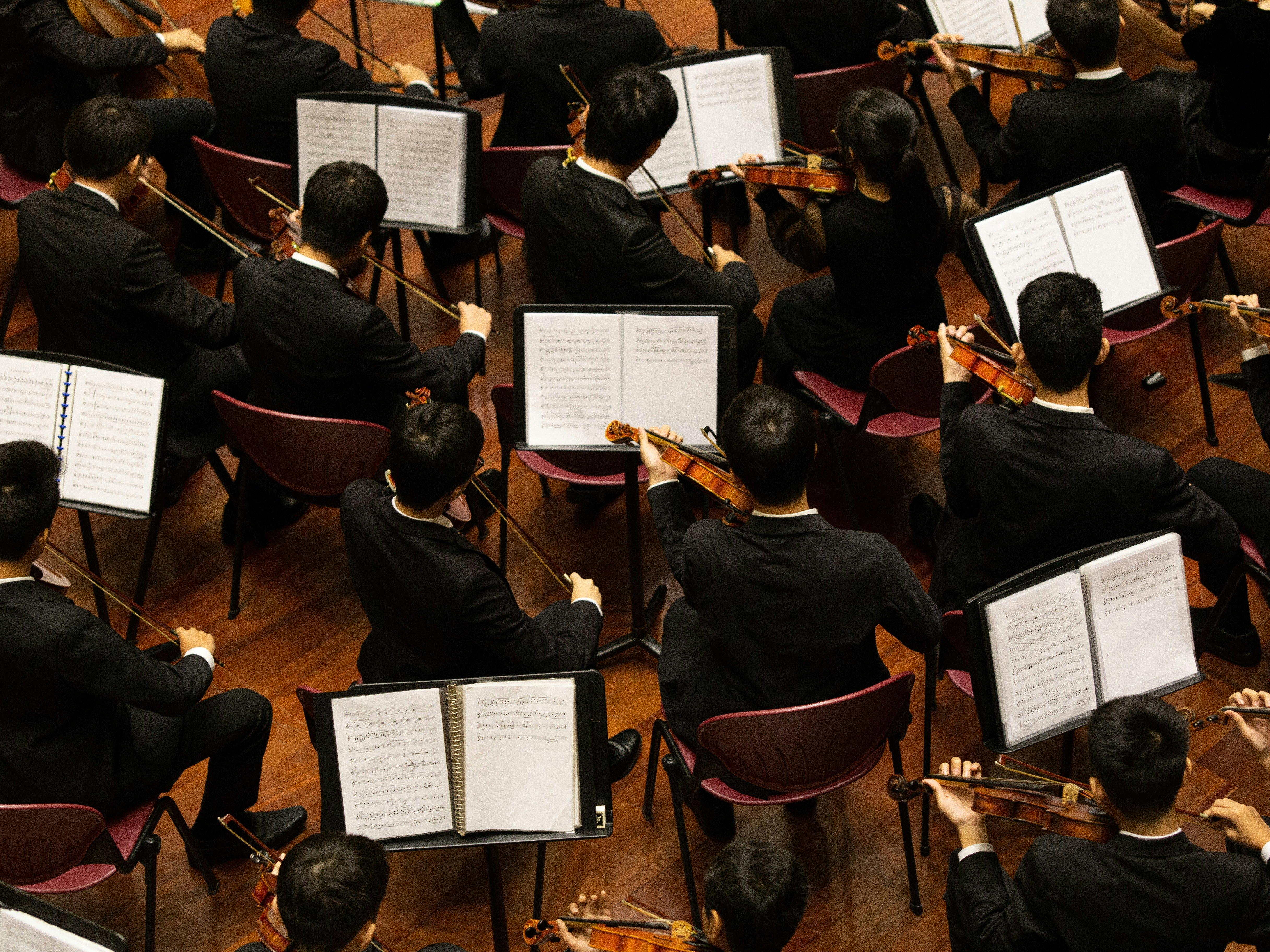 Orchestra musicians in black suits playing string instruments with open sheet music on stands