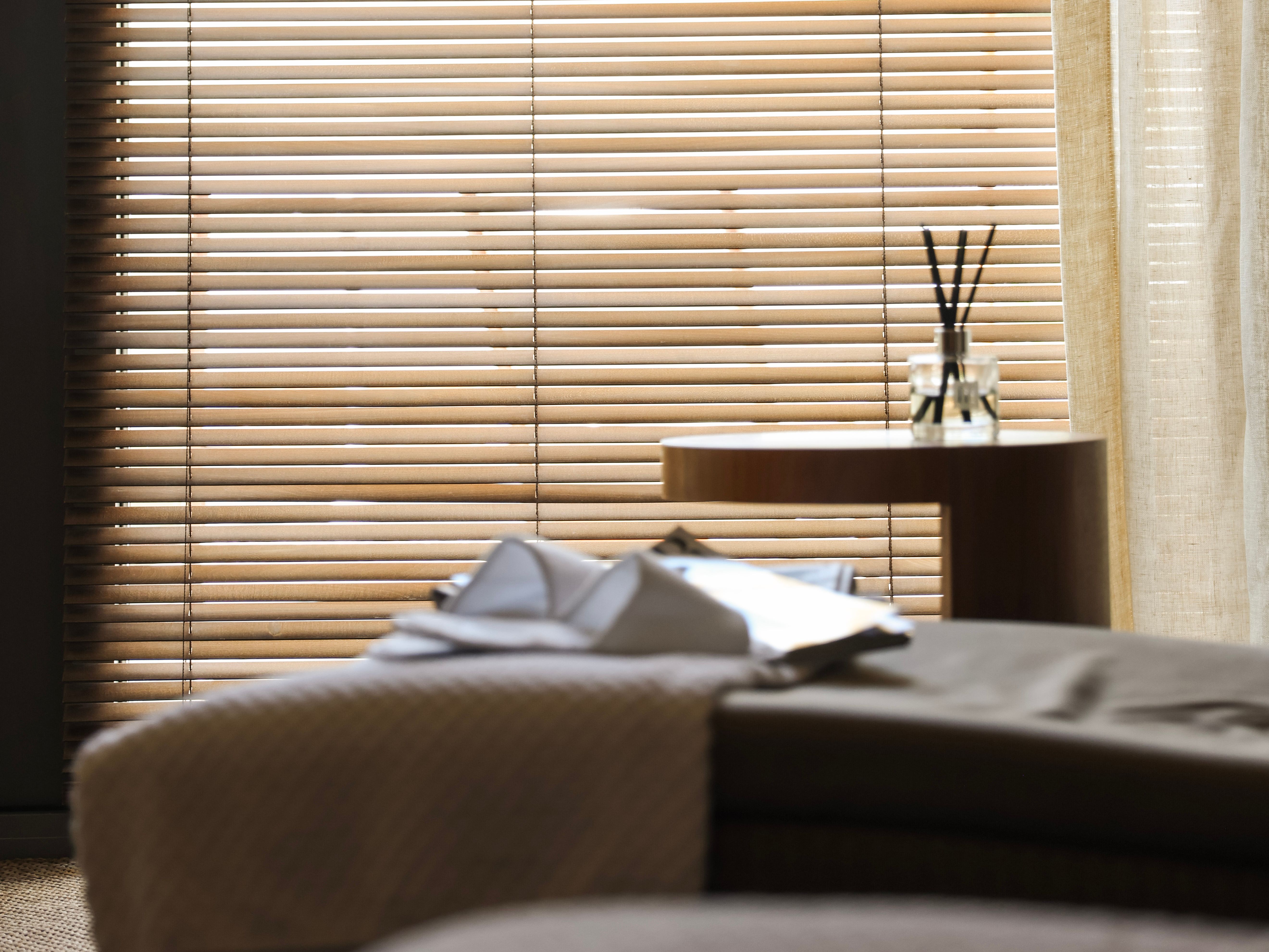 Sunlight filtering through wooden venetian blinds beside a sheer curtain in a bedroom