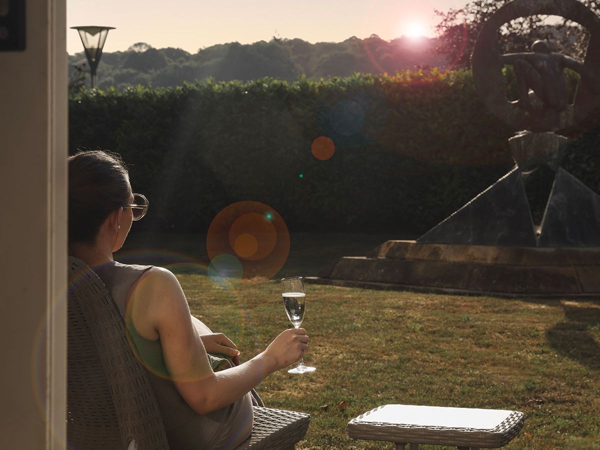 Woman relaxing in a garden chair with a glass of sparkling wine at sunset