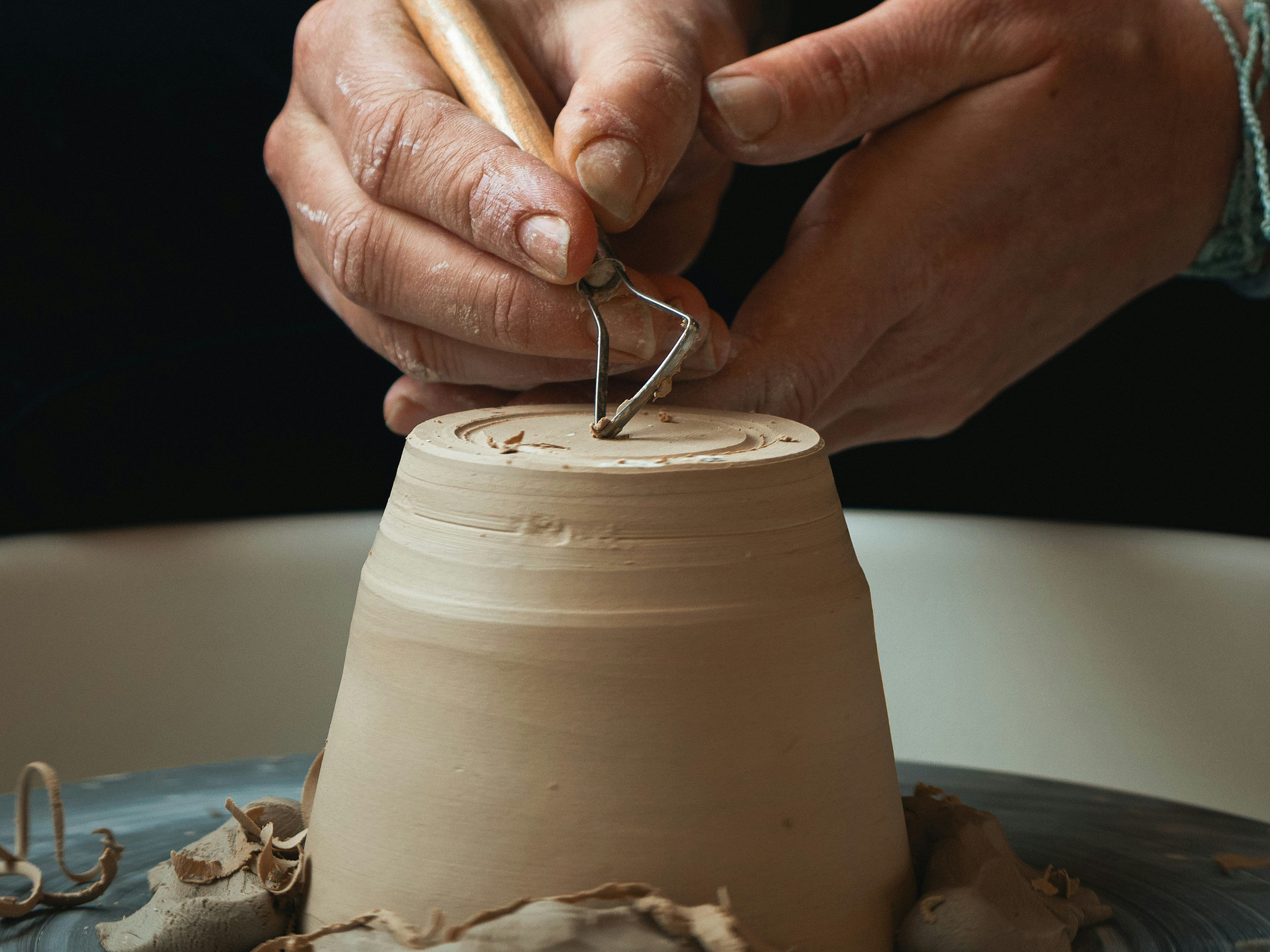 Hands carving a clay pot on a pottery wheel with a sculpting tool
