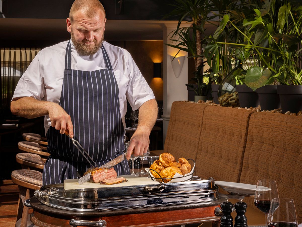 Chef carving roasted meat from a trolley in a restaurant dining room