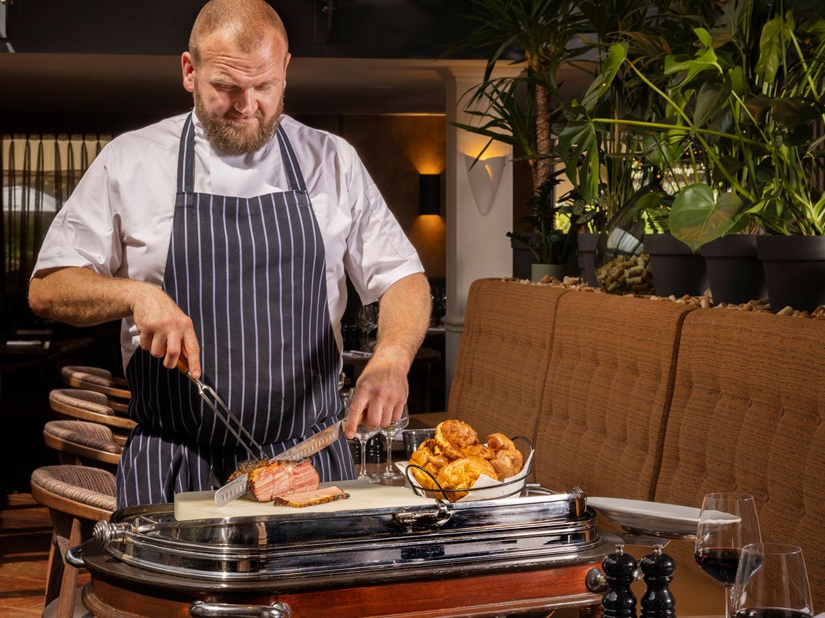 Chef carving roasted meat from a trolley in a restaurant dining room