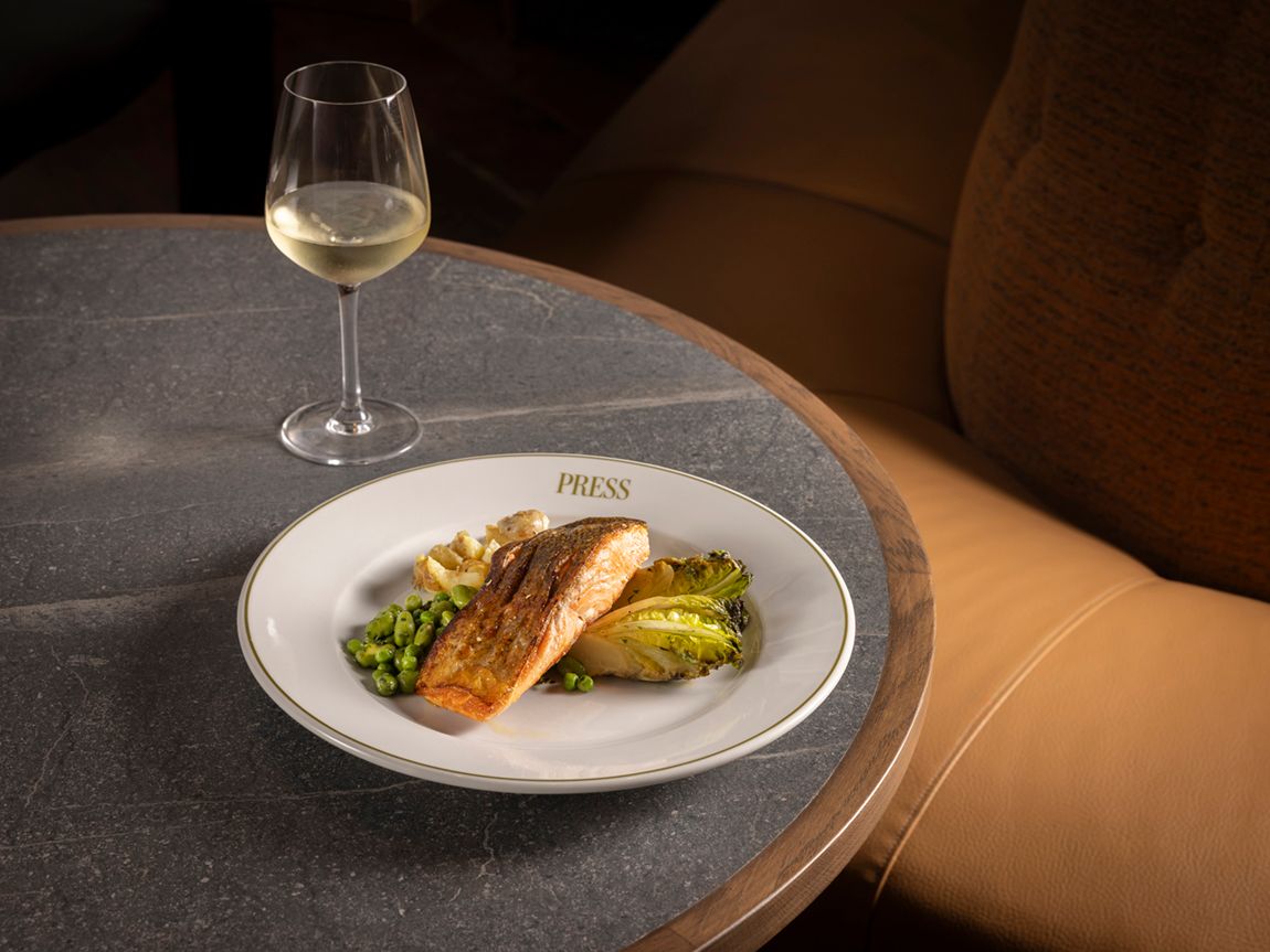 Salmon fillet served with peas and greens on a plate, with a glass of white wine on a table.