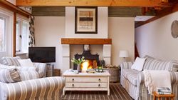 Cosy country-style living room with a wood-burning stove, striped sofas, wooden beams, and a rustic coffee table, creating a warm and inviting atmosphere.
