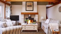 Cosy country-style living room with a wood-burning stove, striped sofas, wooden beams, and a rustic coffee table, creating a warm and inviting atmosphere.