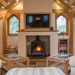 A cosy living room with a wood-burning stove, striped armchairs, wooden beams, and arched windows, creating a warm and inviting countryside retreat.