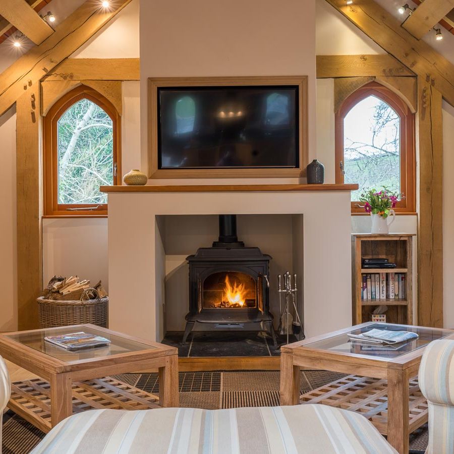 A cosy living room with a wood-burning stove, striped armchairs, wooden beams, and arched windows, creating a warm and inviting countryside retreat.