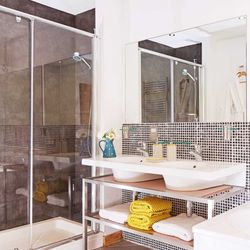 A modern bathroom with a double sink vanity, a glass-enclosed shower, a bathtub, and stylish mosaic tiling, complemented by neatly folded towels and soft lighting.