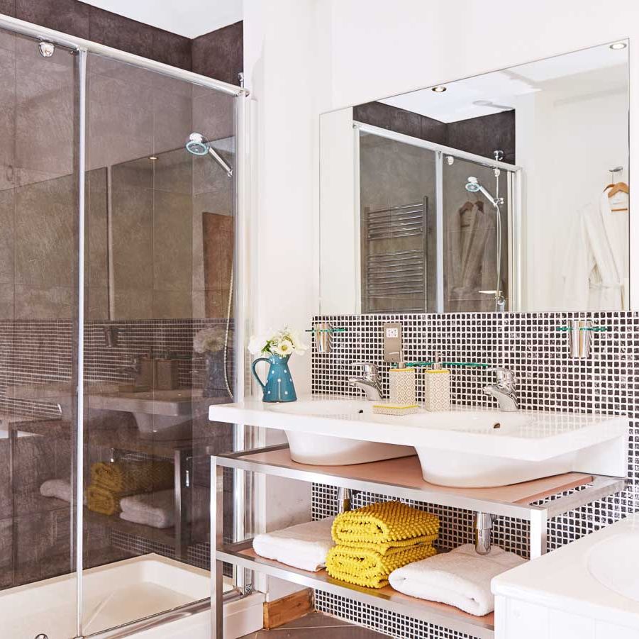 A modern bathroom with a double sink vanity, a glass-enclosed shower, a bathtub, and stylish mosaic tiling, complemented by neatly folded towels and soft lighting.