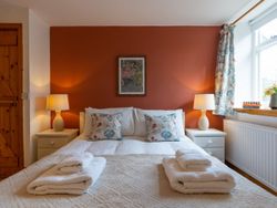 A cosy cottage bedroom with a double bed, warm lighting, a rustic wooden door, and a terracotta accent wall, creating a welcoming and relaxing atmosphere.