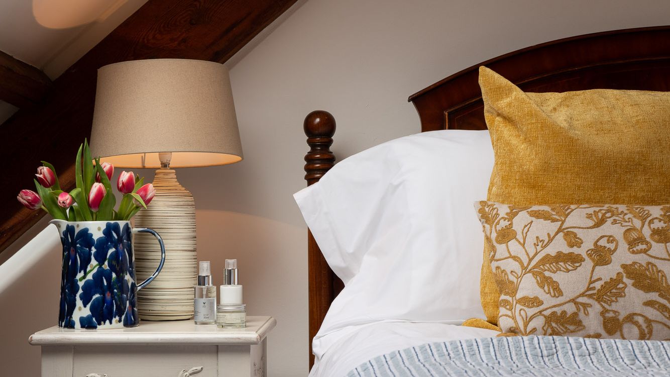 Bed with yellow cushions, vase of tulips on bedside table