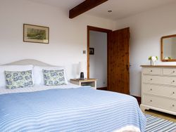 Bright and airy bedroom with a king-size bed, blue and white striped bedding, floral cushions, wooden furniture, and a cosy, rustic charm.