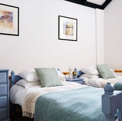 Charming twin bedroom with pastel blue wooden beds, soft green cushions, matching throws, and nautical-themed artwork, creating a cosy and relaxing atmosphere.