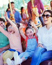 A joyful family rides a vintage carousel, with children raising their hands in excitement. The brightly colored horses and ornate decorations add to the festive atmosphere.