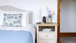 Bed with blue throw, vase of wildflowers on bedside table