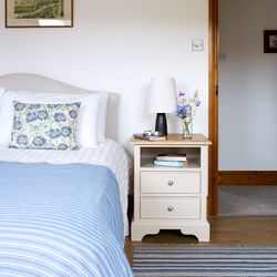 Bed with blue throw, vase of wildflowers on bedside table