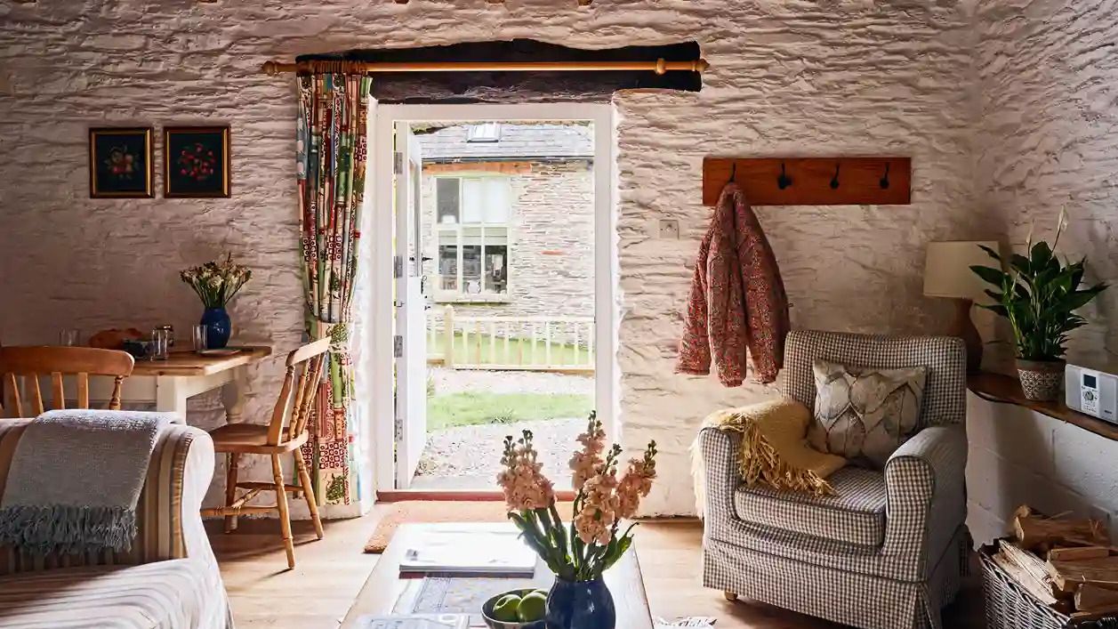 Charming interior of 1843 at Flear Farm Cottages, with exposed beams, armchair, dining nook, and open doors leading to the garden.