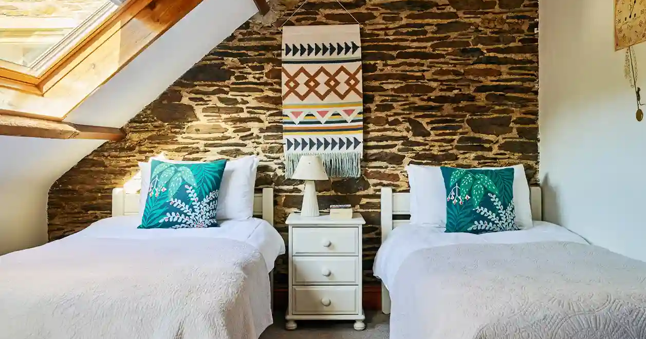 Twin bedroom in Cartwheel at Flear Farm Cottages, with exposed stone wall, skylight, white bedding, and bold green cushions for a fresh touch.