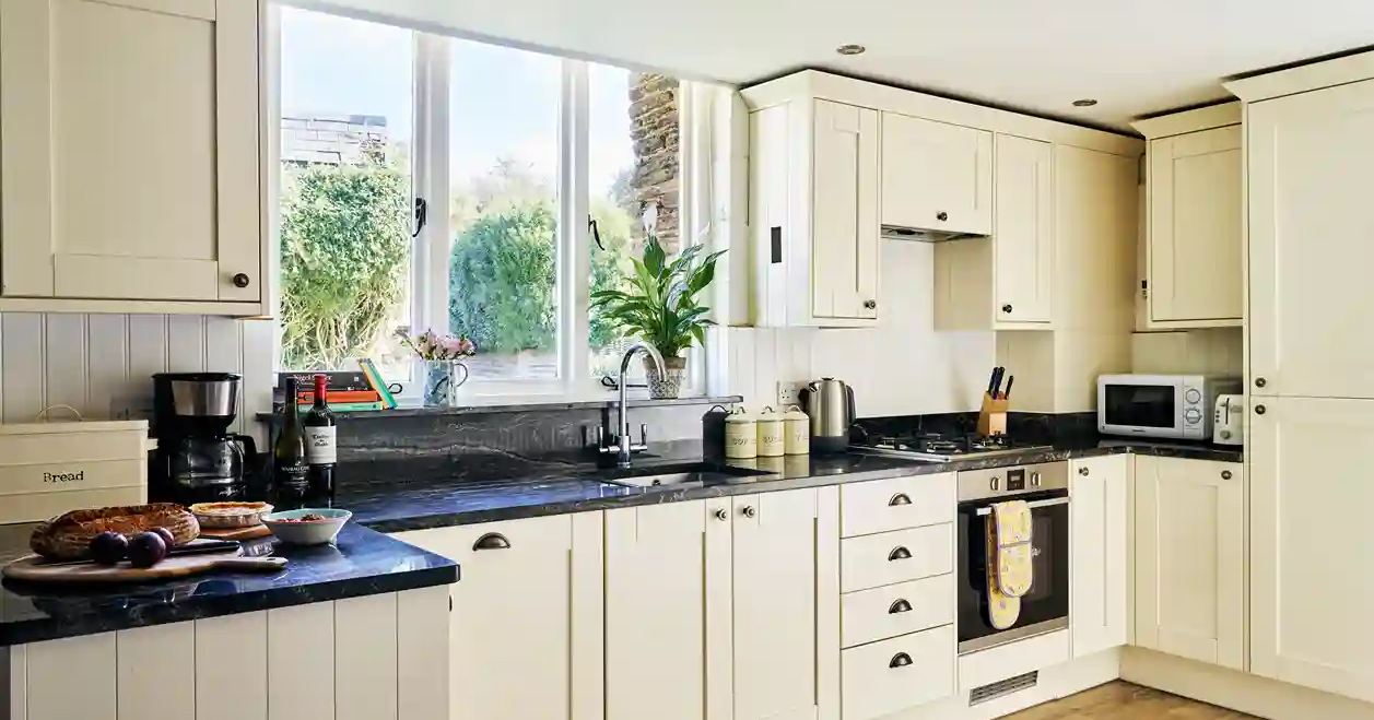 Kitchen in the Granary at Flear Farm Cottages, with cream shaker units, black worktops, large window, and fresh bread and wine on the counter.