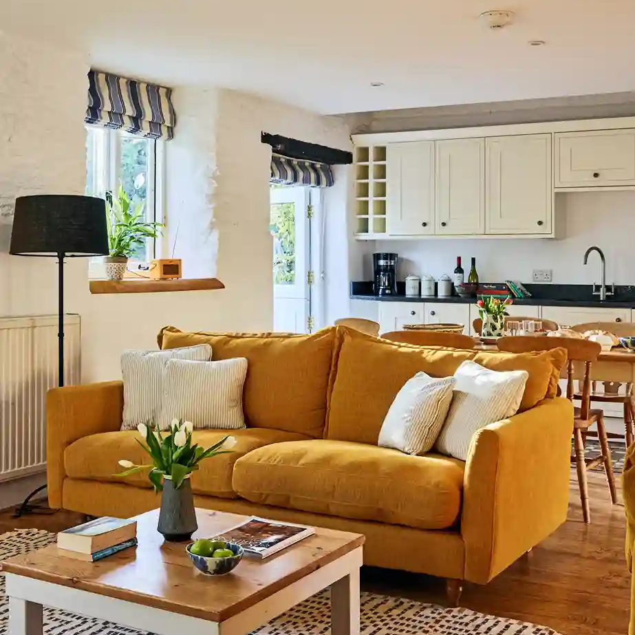 Cosy living room in The Stables at Flear Farm Cottages with mustard sofa, striped blinds, and open-plan kitchen and dining area.