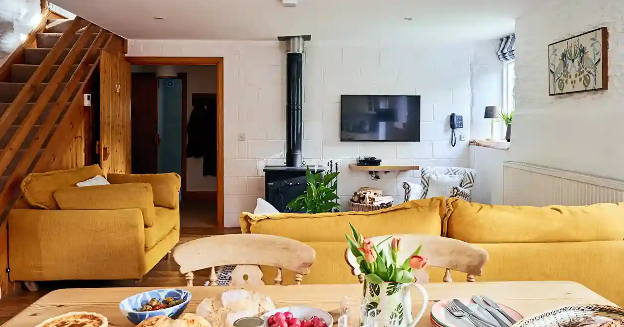 View from the kitchen table to the living room in The Stables at Flear Farm Cottages, with mustard sofas and a wood-burning stove.