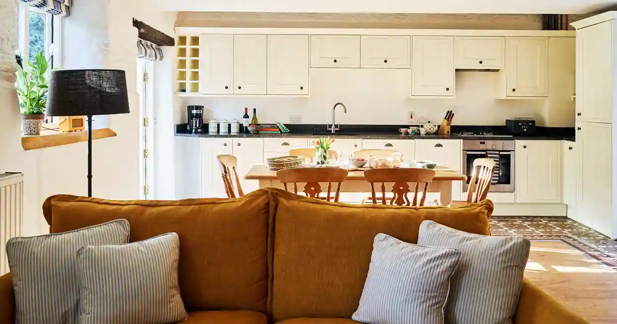 The Stables at Flear Farm Cottages, with a mustard sofa in the foreground and cream shaker-style kitchen with dining table in the background.