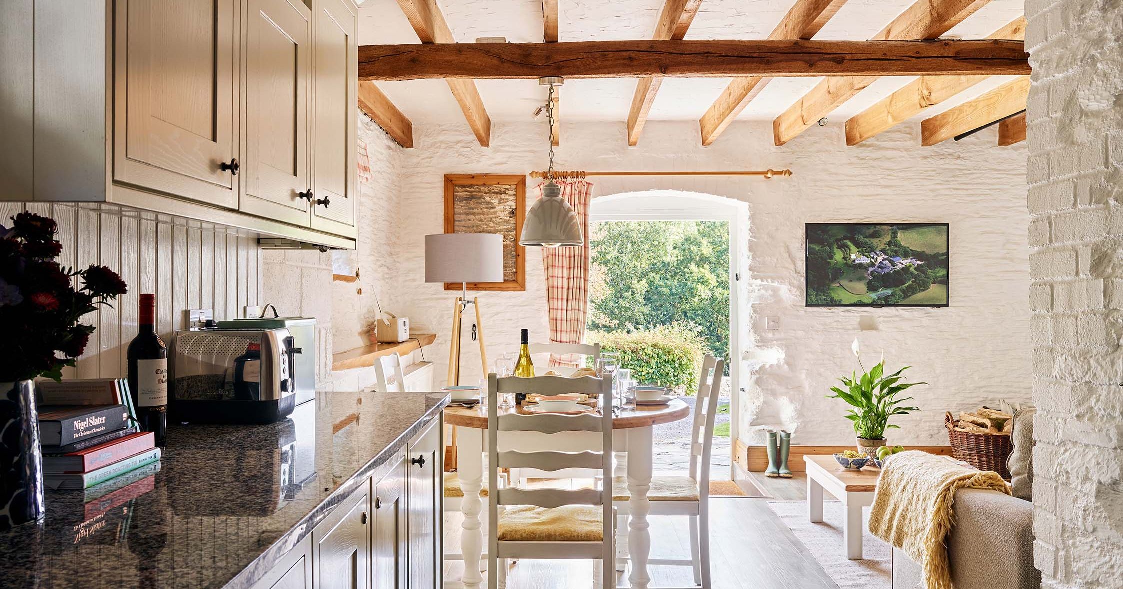 View from Quarry’s kitchen at Flear Farm Cottages through the dining area to open doors, showing the sunlit garden beyond.