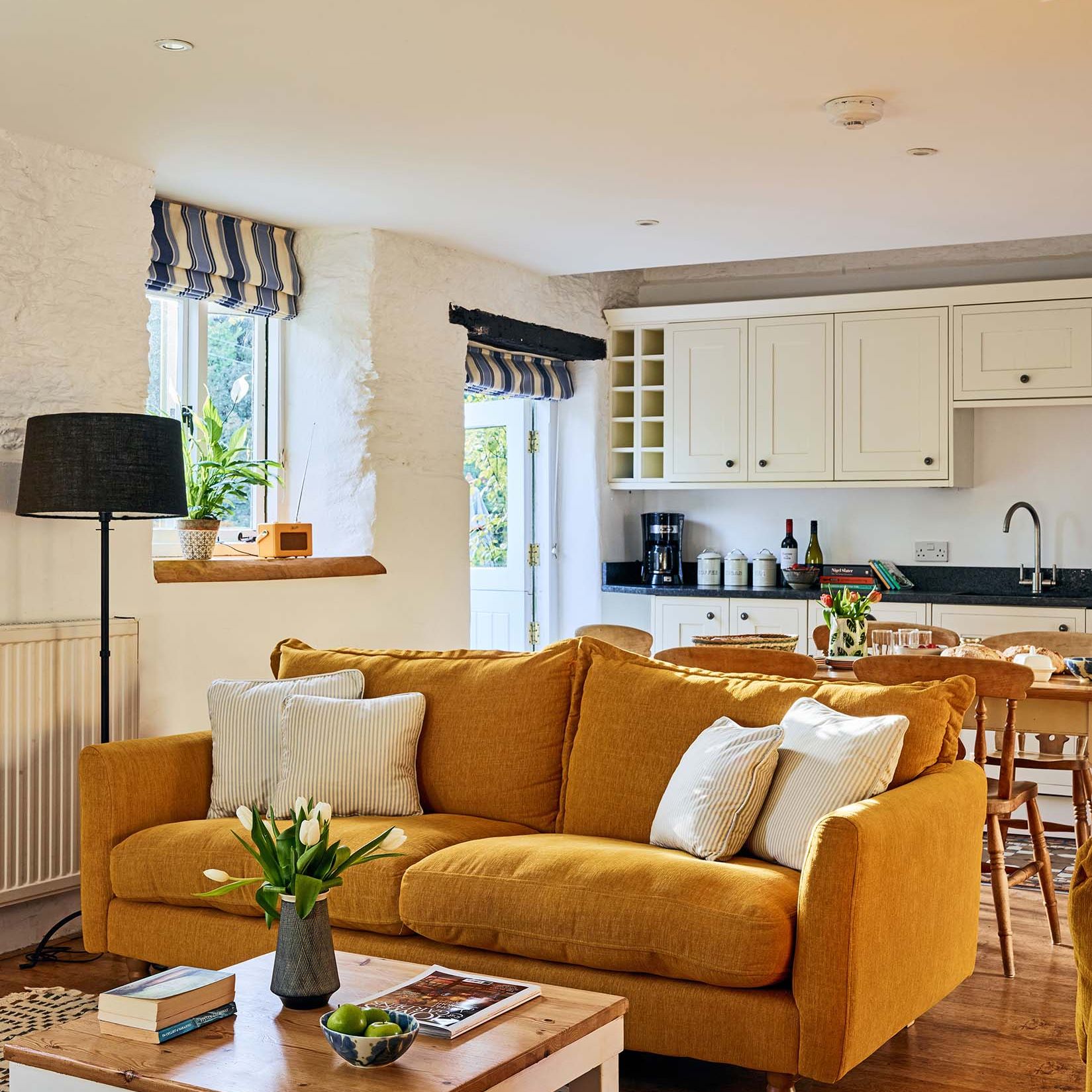 Cosy living room in The Stables at Flear Farm Cottages with mustard sofa, striped blinds, and open-plan kitchen and dining area.
