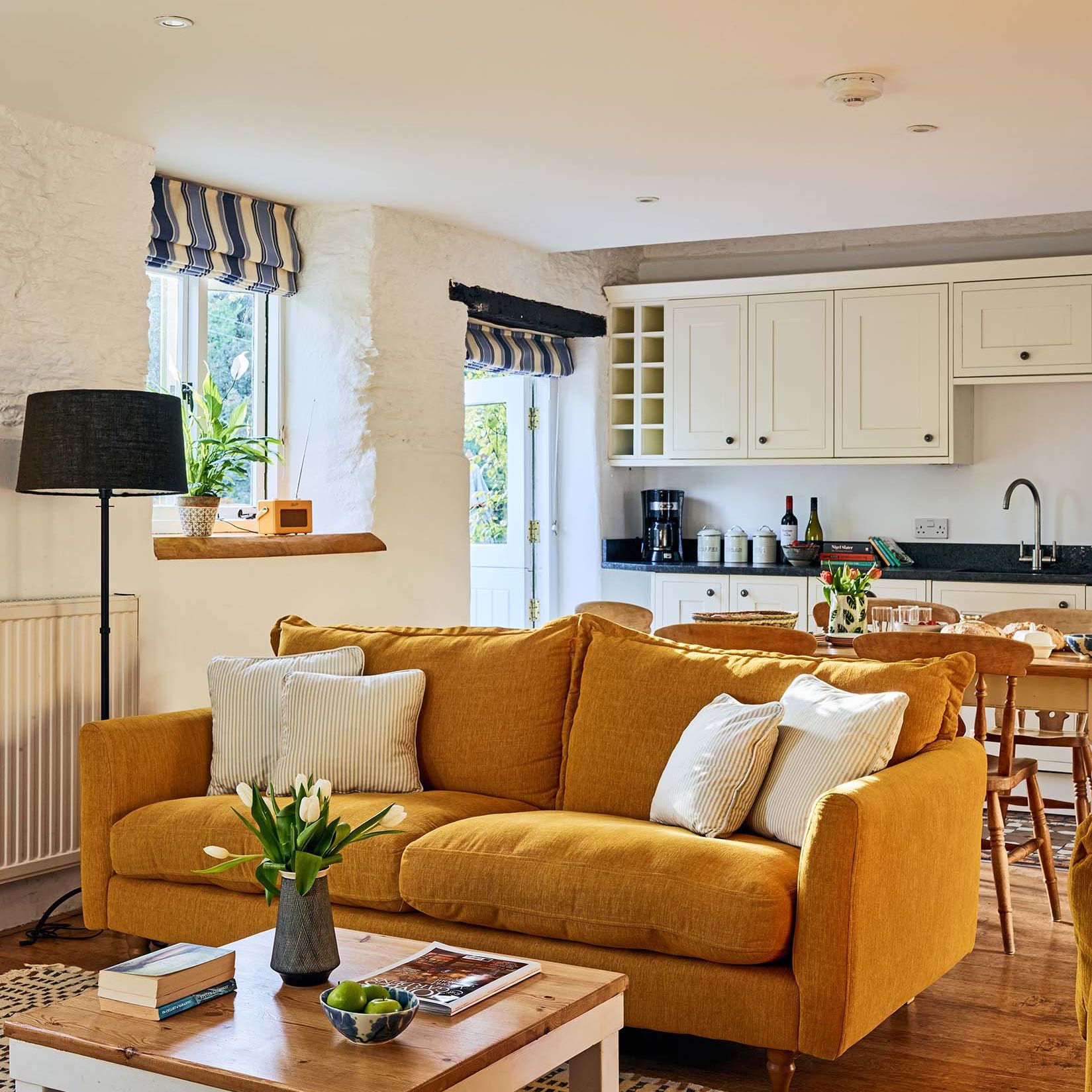 Cosy living room in The Stables at Flear Farm Cottages with mustard sofa, striped blinds, and open-plan kitchen and dining area.