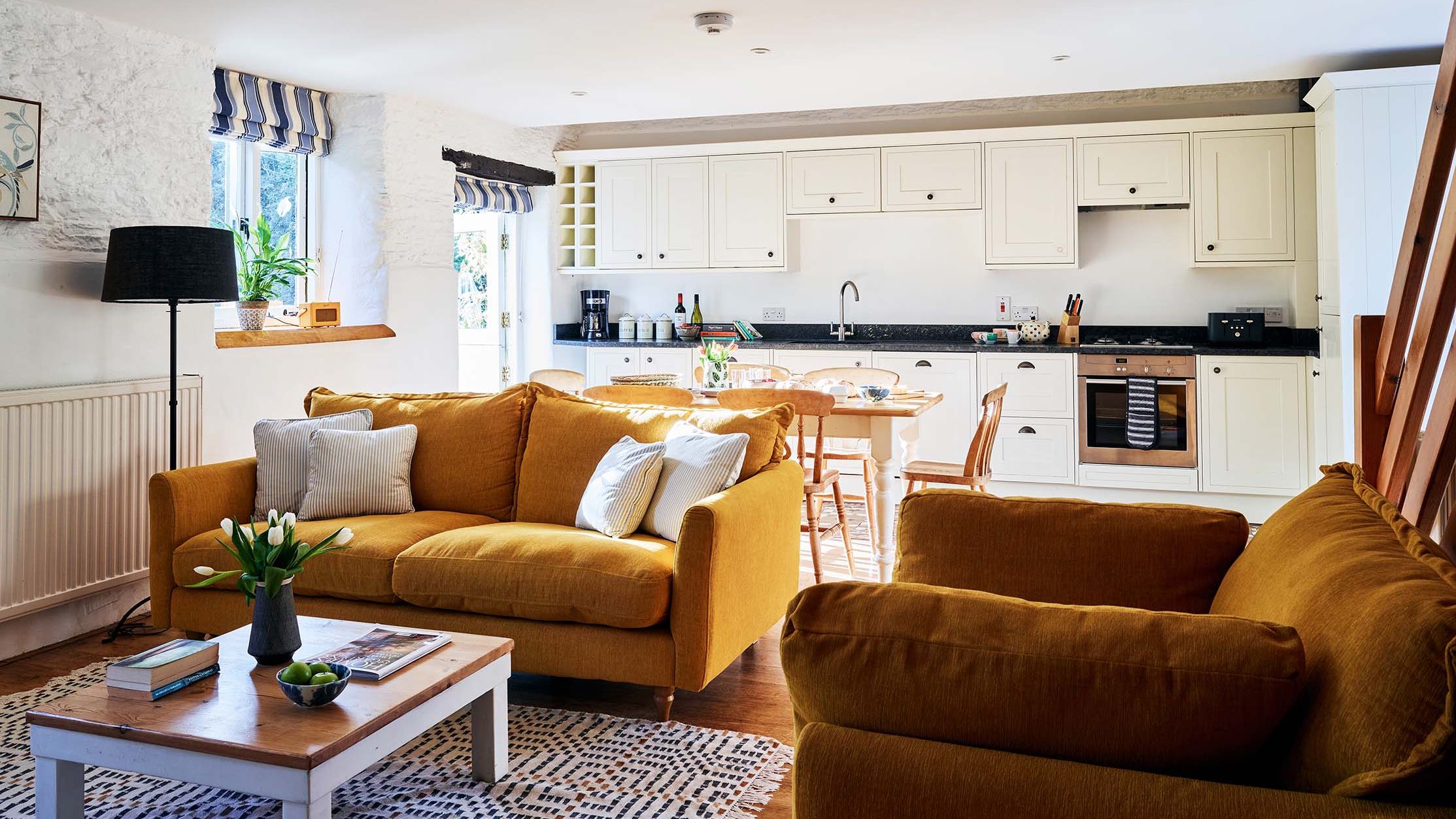 Open-plan living room and kitchen in The Stables at Flear Farm Cottages, with mustard sofas, cream cabinetry and a wooden dining table.