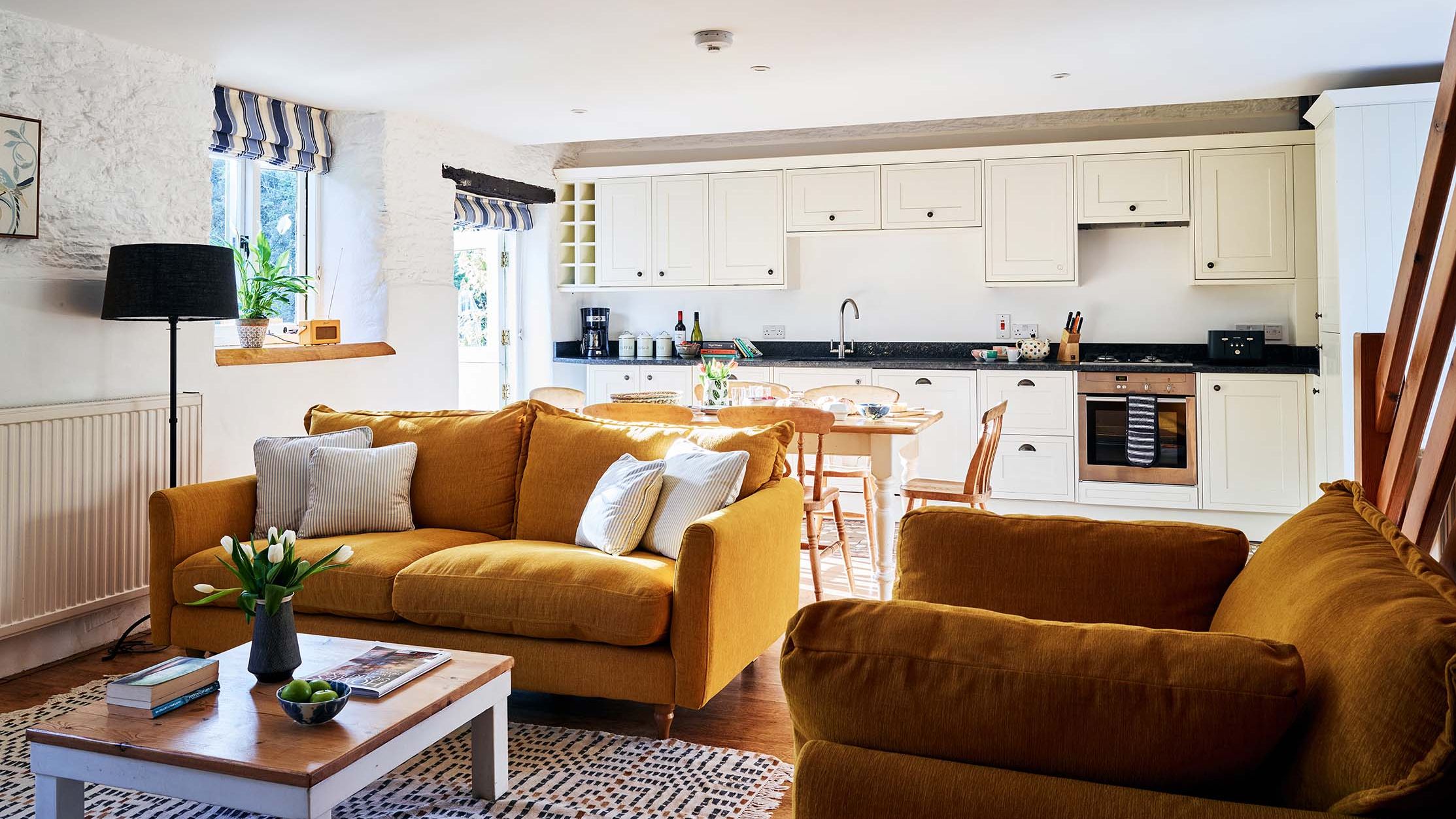 Open-plan living room and kitchen in The Stables at Flear Farm Cottages, with mustard sofas, cream cabinetry and a wooden dining table.