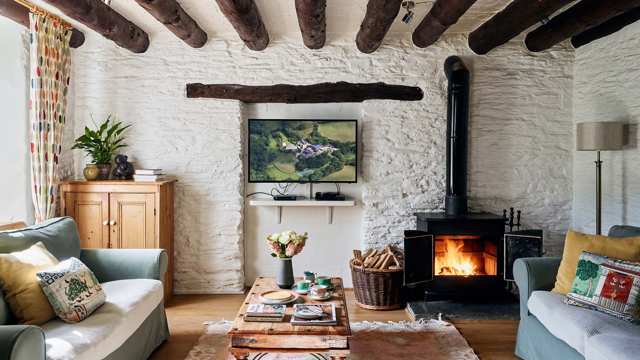 Cosy living room in the Granary at Flear Farm Cottages, with wood burner, soft sofas, rustic coffee table, exposed beams, and colourful cushions.