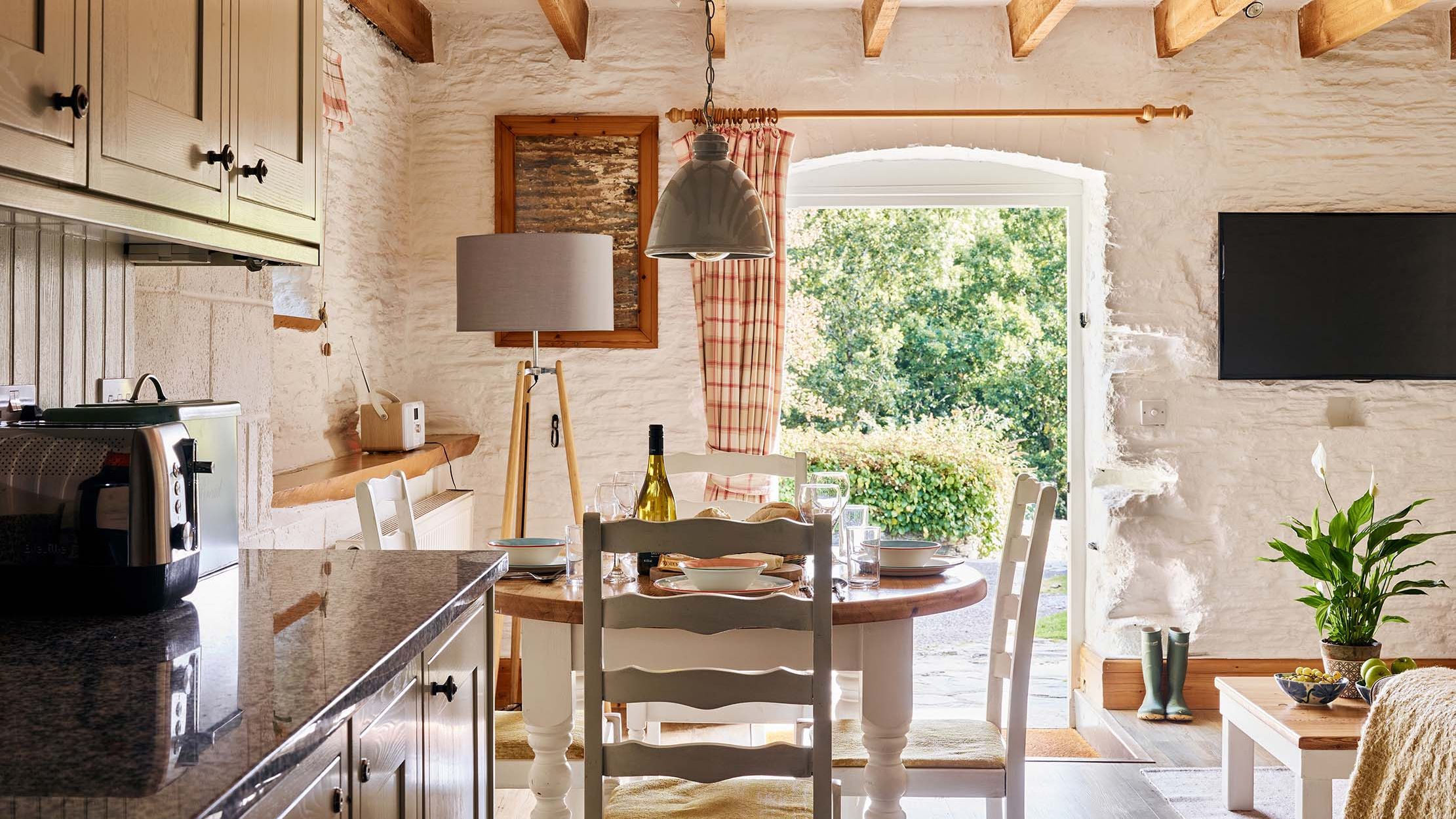 View from Quarry’s kitchen at Flear Farm Cottages through the dining area to open doors, showing the sunlit garden beyond.