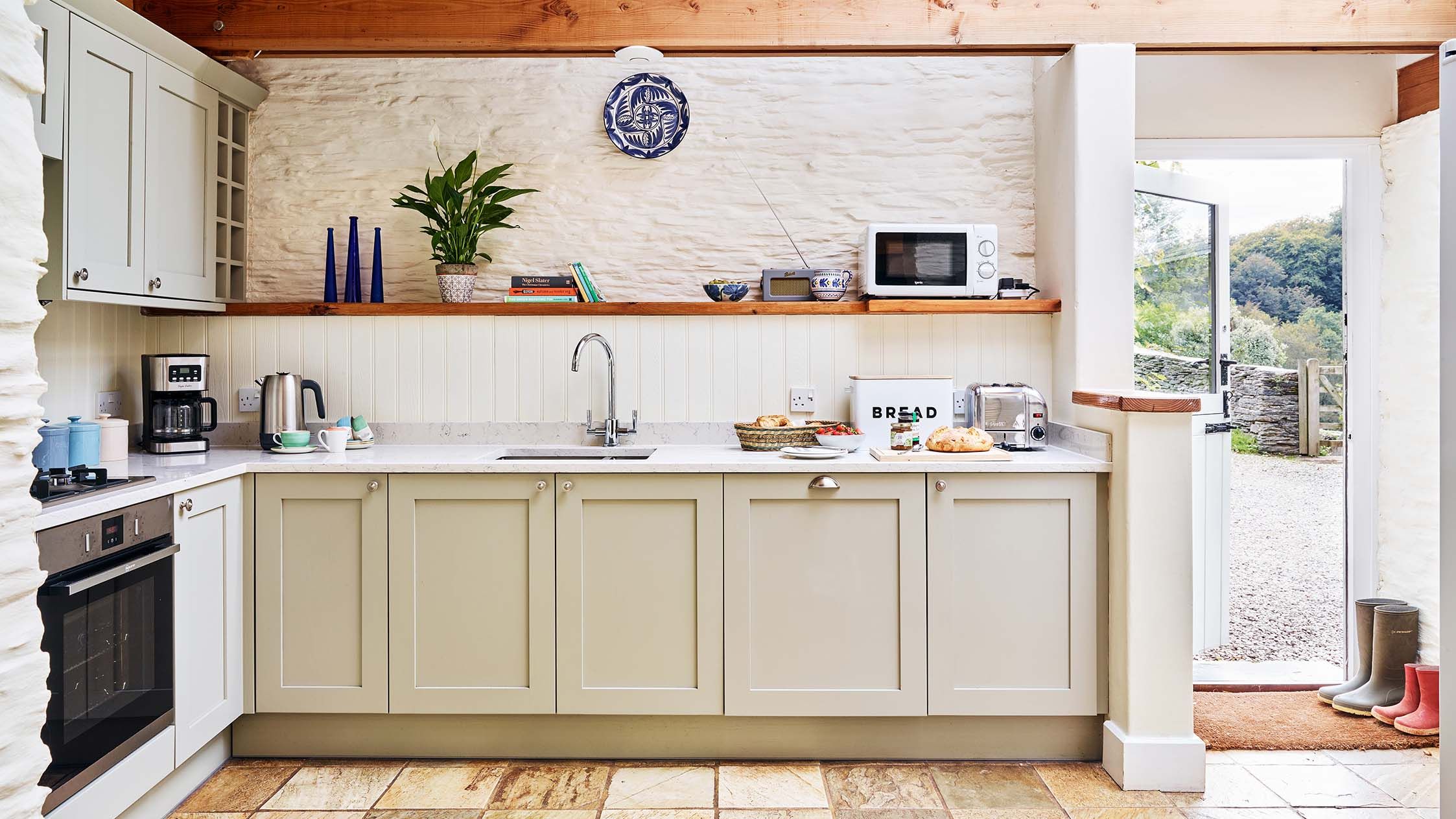Light-filled kitchen in The Linhay at Flear Farm Cottages with pale units, wooden beams, and a door opening to the countryside.