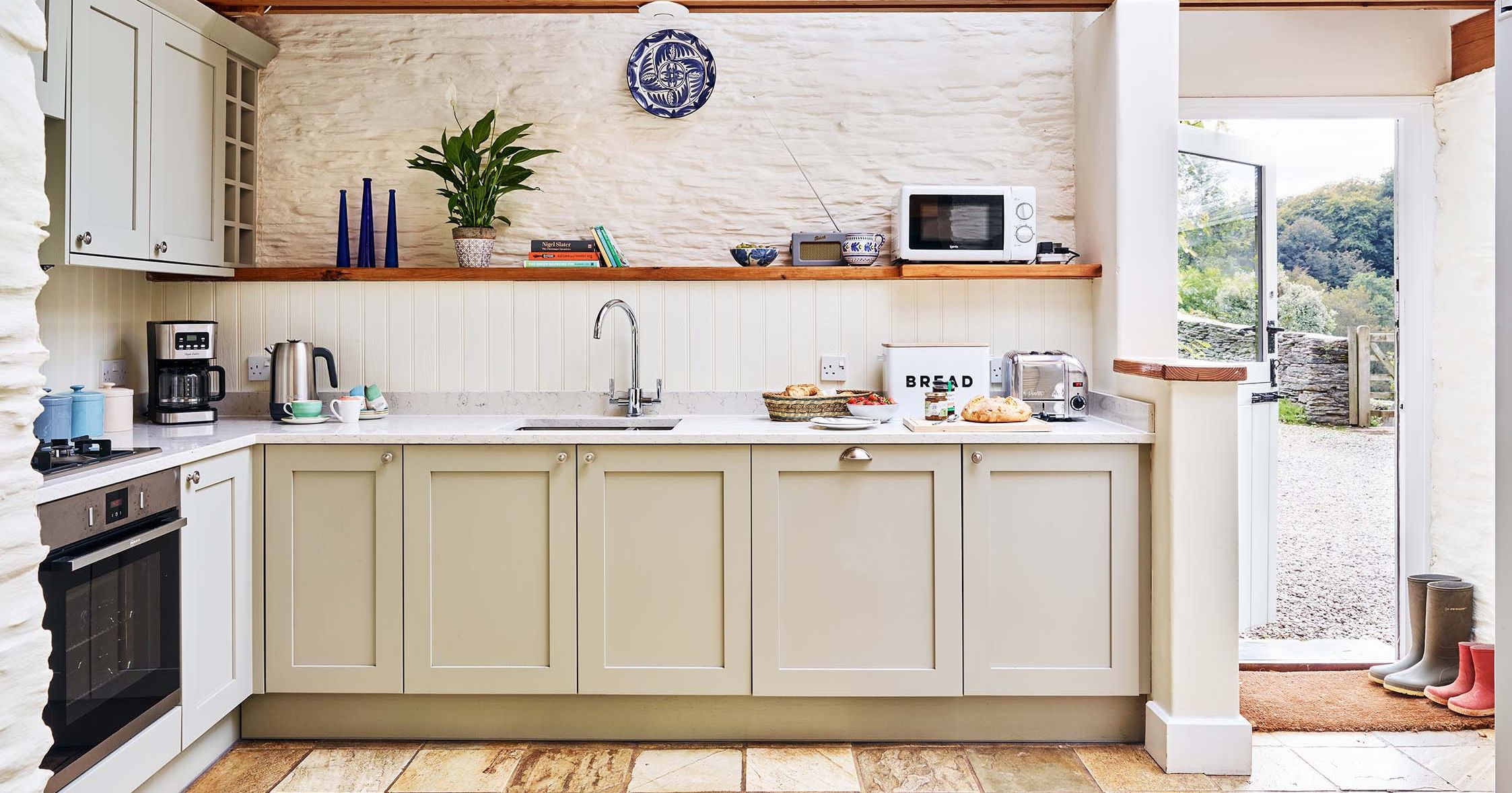 Light-filled kitchen in The Linhay at Flear Farm Cottages with pale units, wooden beams, and a door opening to the countryside.