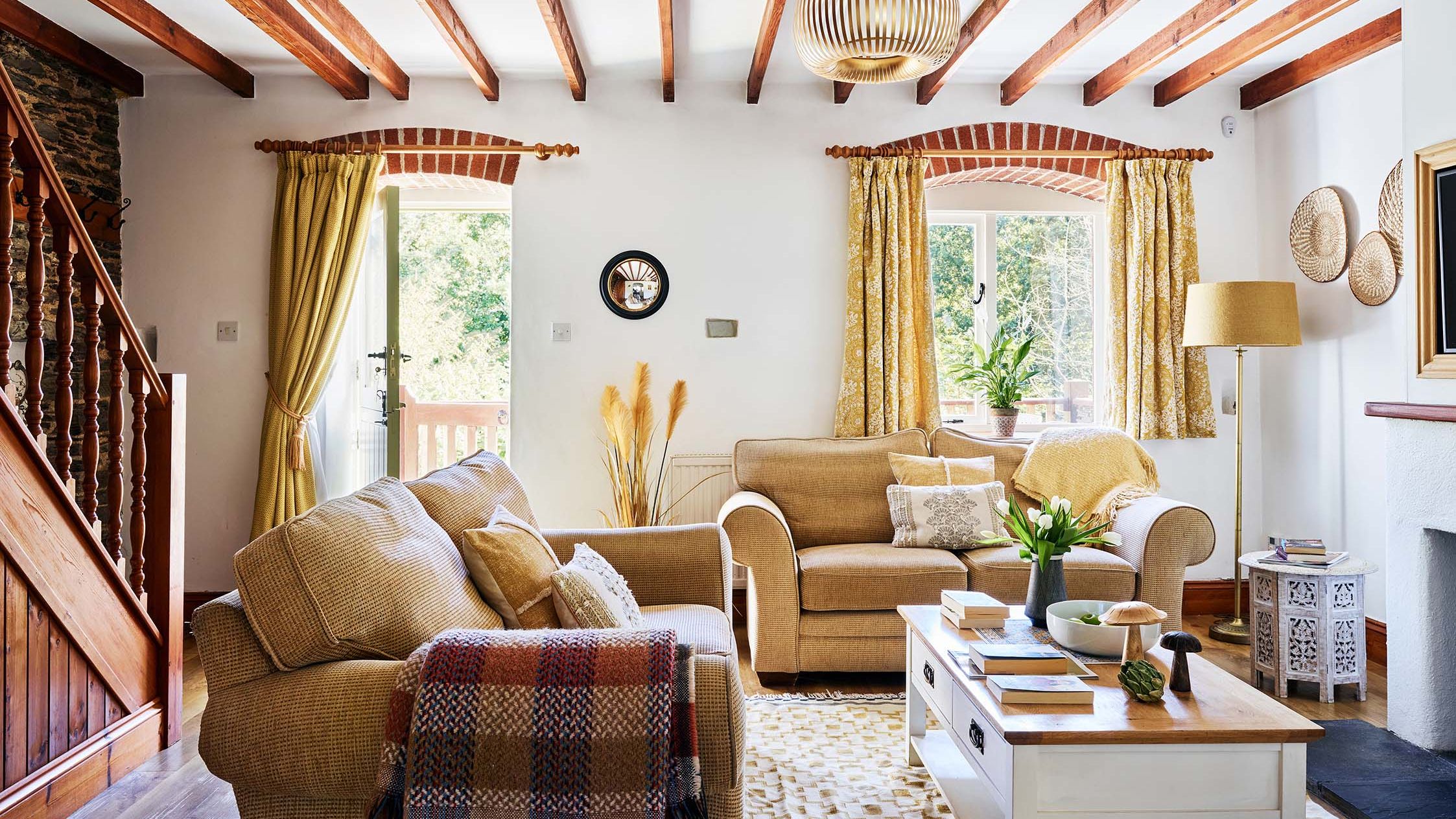 Inviting lounge in Cartwheel at Flear Farm Cottages, with exposed beams, soft sofas, yellow curtains, a wood burner, and open staircase.
