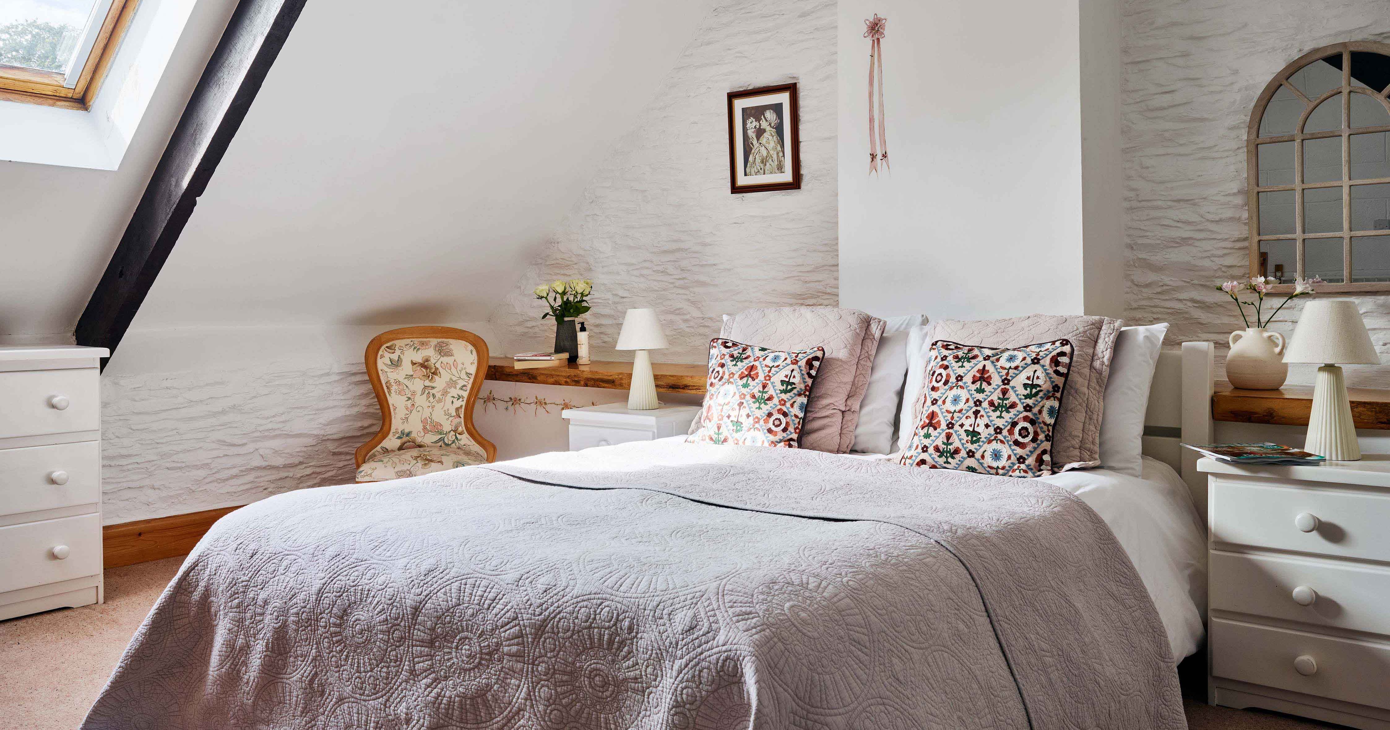 Master bedroom in 1843 at Flear Farm Cottages with a skylight, decorative cushions, soft grey bedding, and vintage-style furniture.