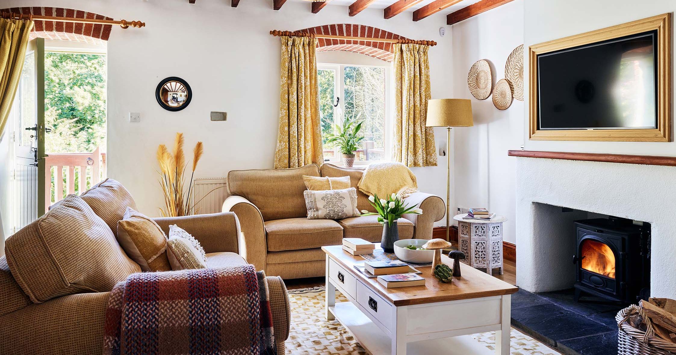 Cosy lounge in Cartwheel at Flear Farm Cottages with exposed beams, soft neutral sofas, a wood burner, and bright yellow accents throughout.