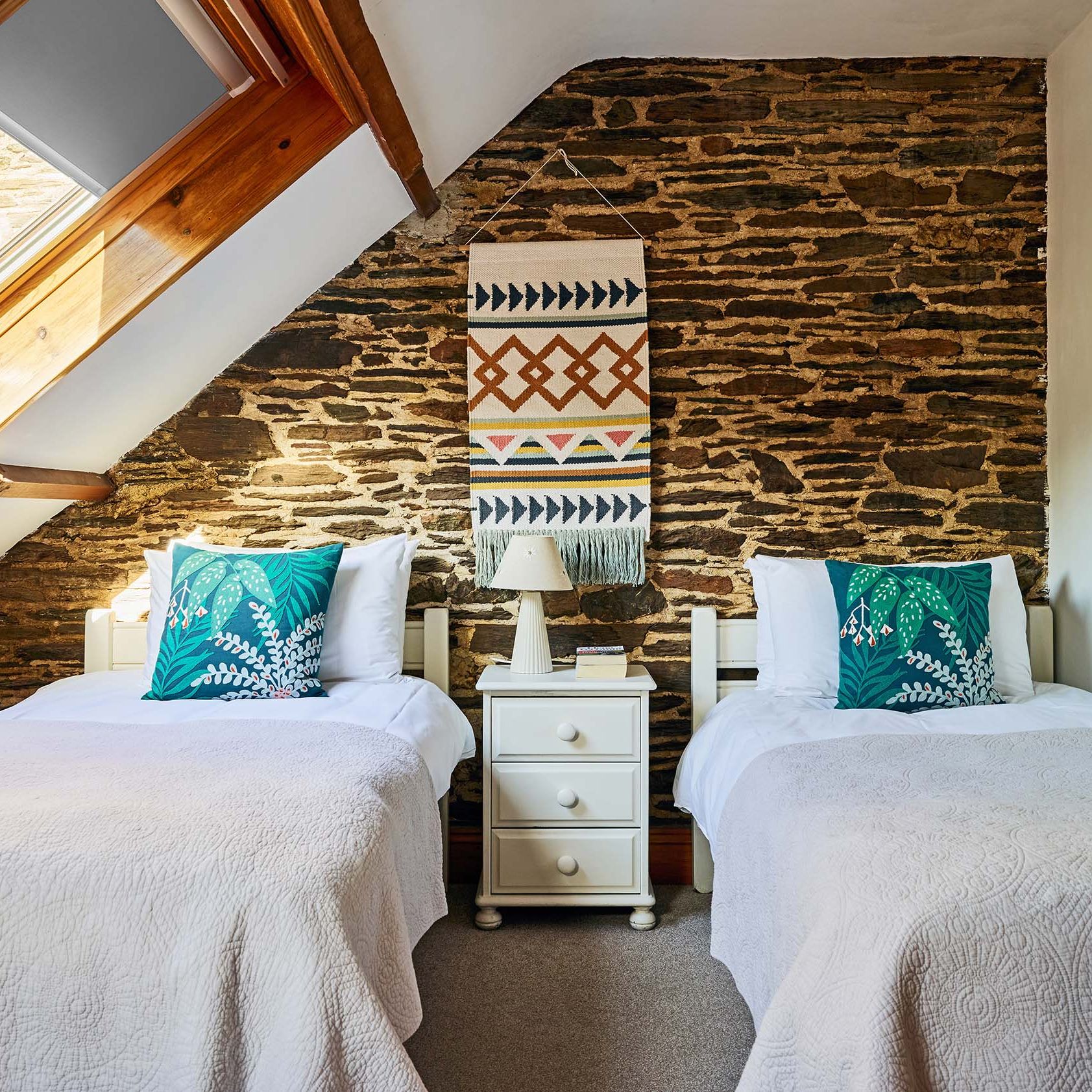 Twin bedroom in Cartwheel at Flear Farm Cottages, with exposed stone wall, skylight, white bedding, and bold green cushions for a fresh touch.