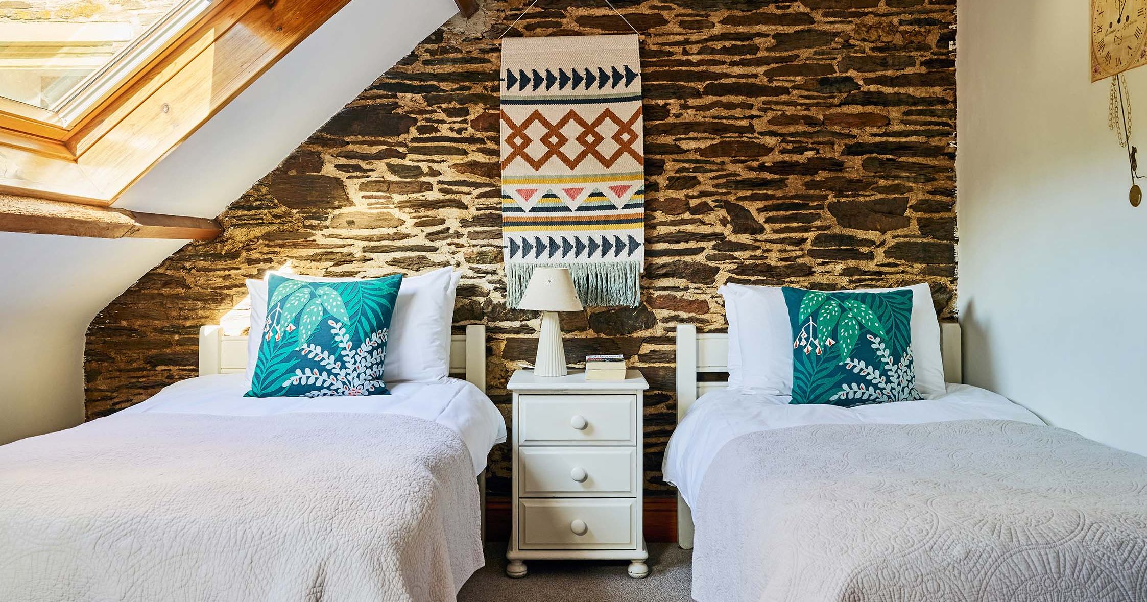 Twin bedroom in Cartwheel at Flear Farm Cottages, with exposed stone wall, skylight, white bedding, and bold green cushions for a fresh touch.